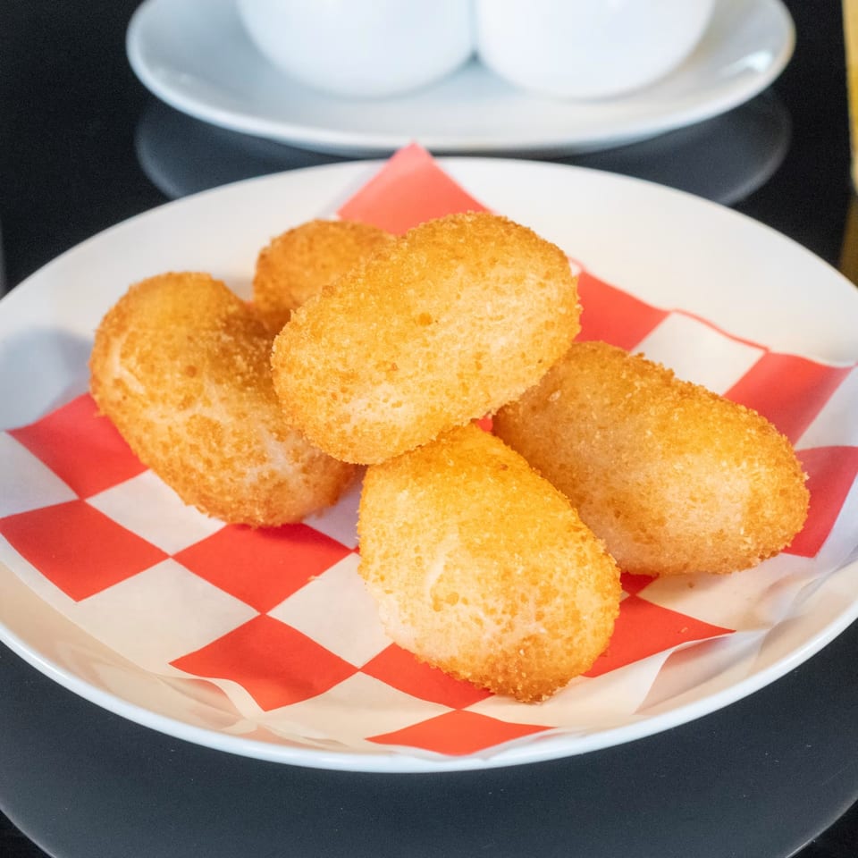 Five golden-brown fried shrimp balls on a white plate with red and white checkered paper.