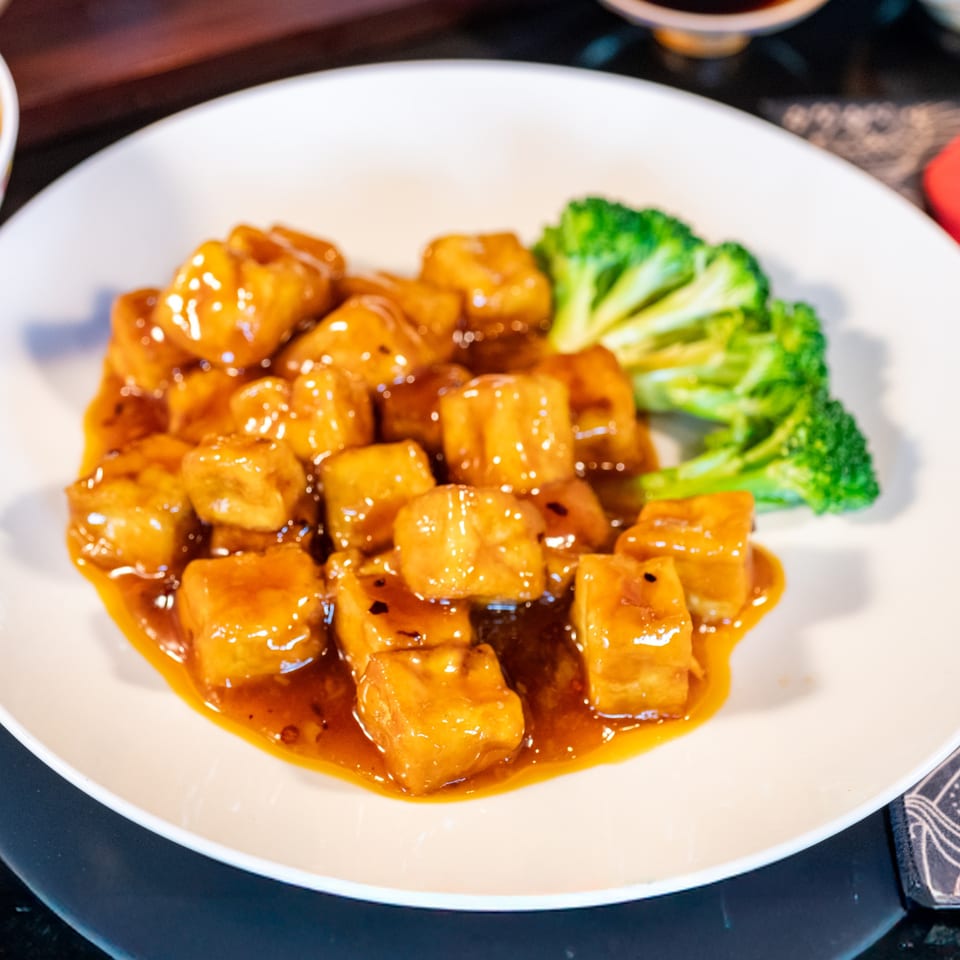 Sweet and sour tofu with broccoli florets on a white plate at Bamboo House.