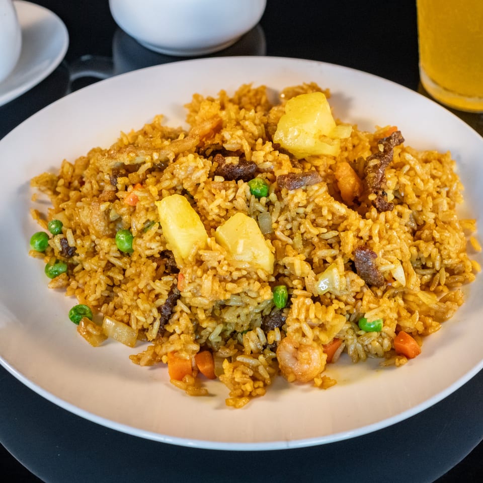Pineapple fried rice with beef, shrimp, peas, and carrots on a white plate.