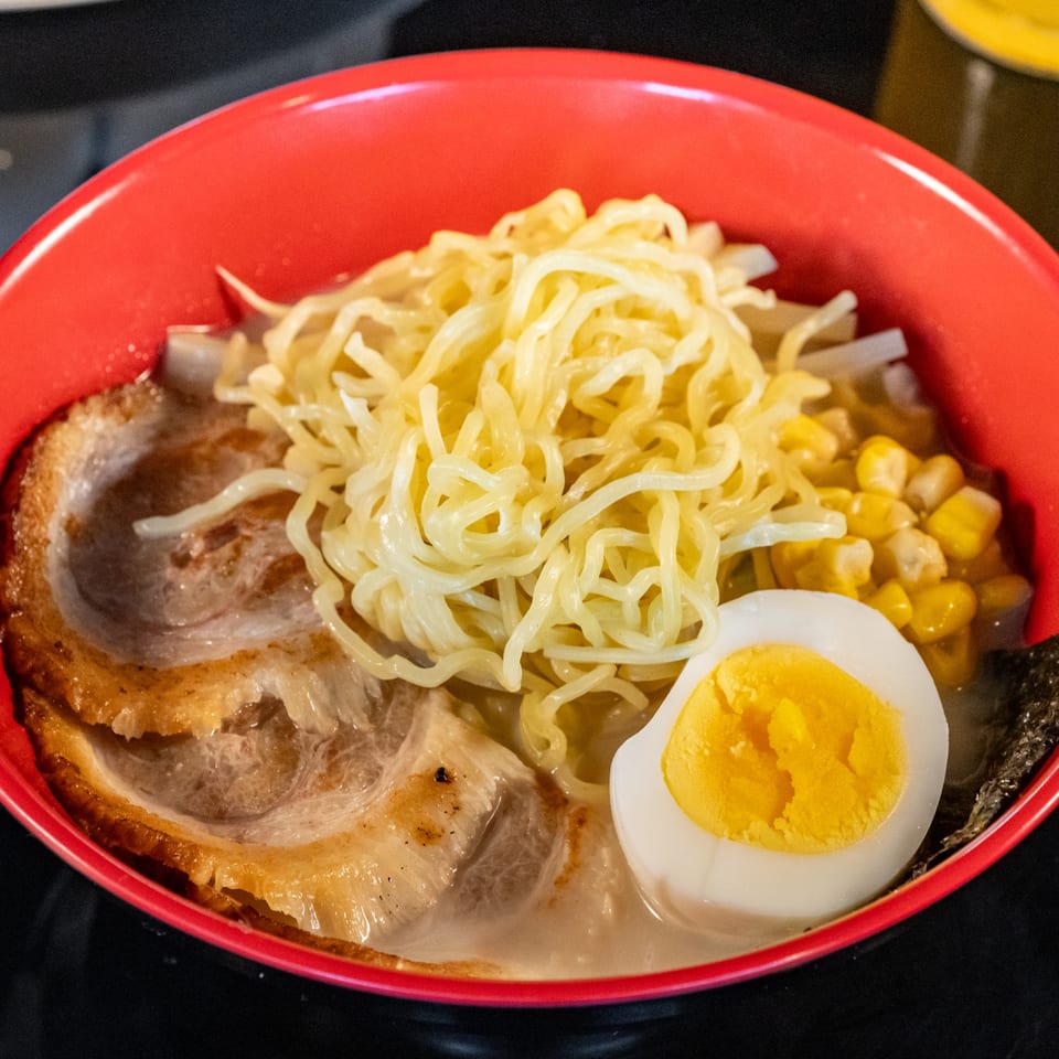 A red bowl of ramen with pork, noodles, corn, and a hard-boiled egg.