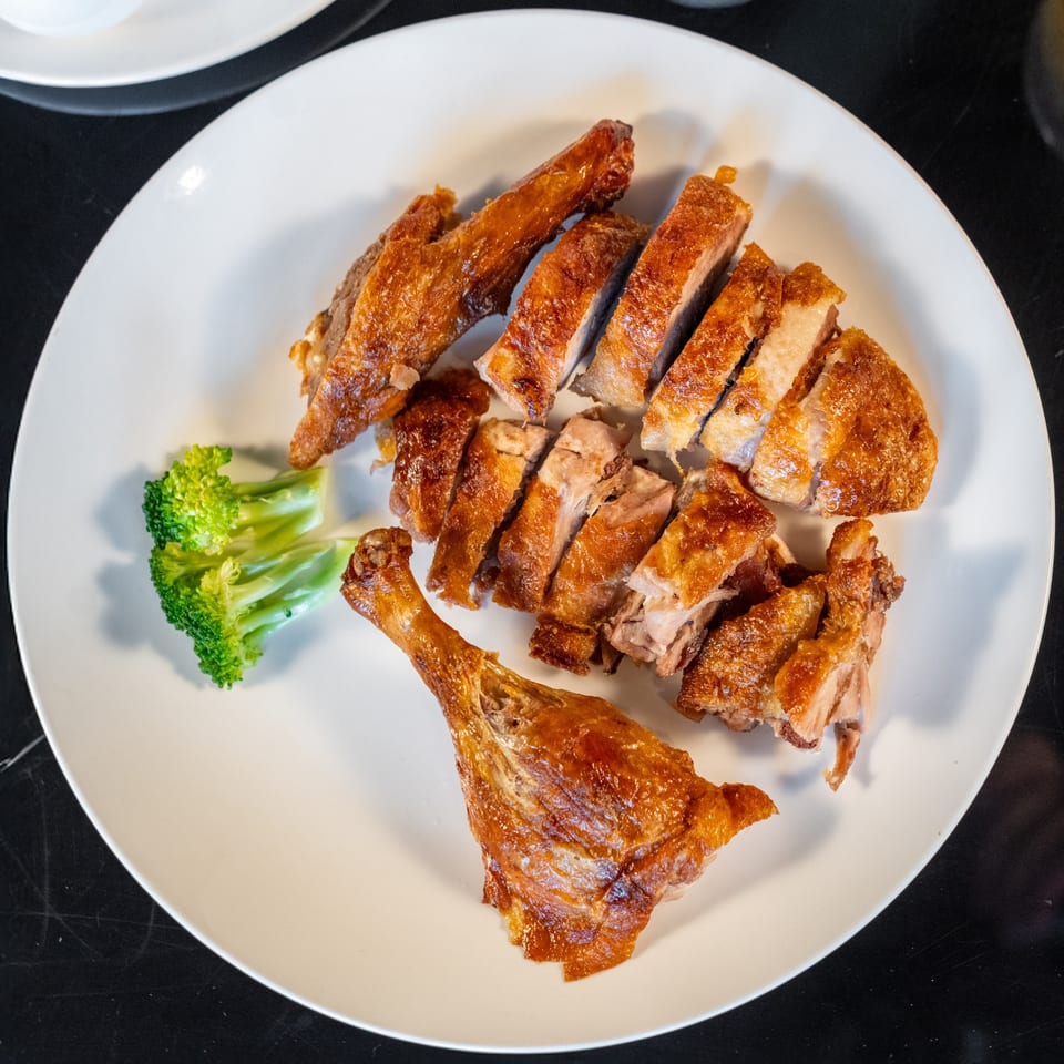 Crispy Peking duck, sliced and served with a side of broccoli on a white plate.