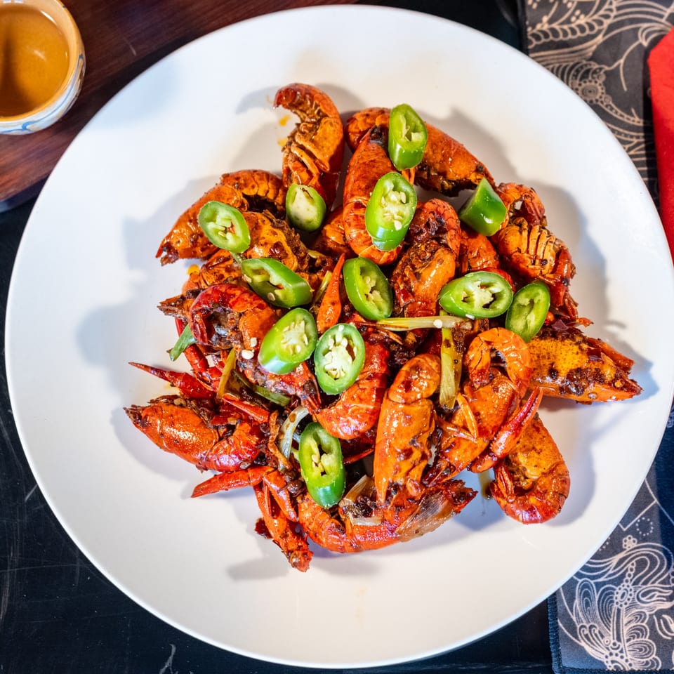 A white plate filled with spicy Chinese crawfish, garnished with green chili slices and scallions.
