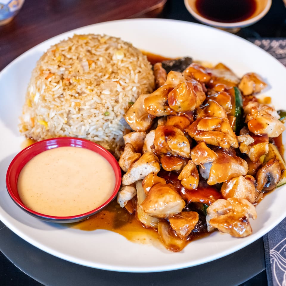 A plate of Bamboo House's General Tso's chicken with fried rice and a side of sauce.